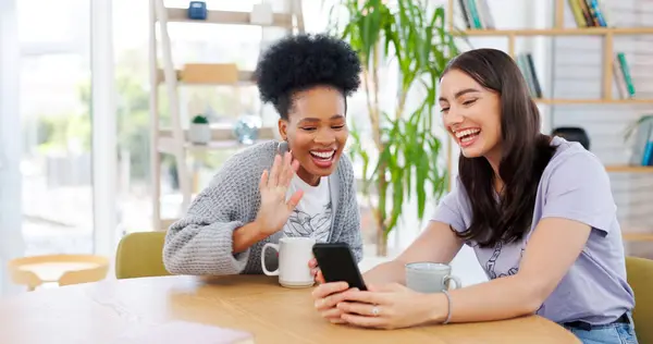 Women friends, video call and phone in coffee shop, wave and excited for conversation, talk and contact. Girl, smartphone and smile together for communication, social media app and relax with tea cup.