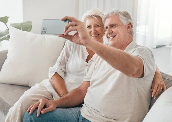 Happy, selfie and old couple on sofa in home, living room or apartment in retirement with post on social media. Mature, people and smile in profile picture, live stream or video call with smartphone.