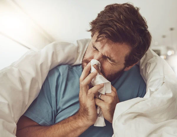 Man, blowing nose and sneezing, sick with allergies or influenza, virus and bacteria with health fail at home. Toilet paper, illness and healthcare with crisis or blanket, medical condition and flu.