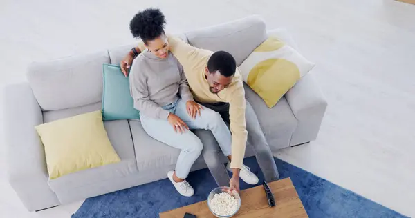 Couple, watching tv and eating popcorn in home, living room and date in apartment with comedy or movies. Happy, people and together on sofa with food to watch tv show or film or above lounge in house.