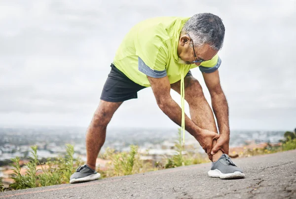 Mature, man and stretch from exercise by road for recovery, wellness or joint pain for better health. Elderly person, fitness or workout for strength, power or cardio for rehabilitation in retirement.