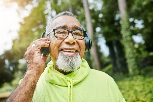 Mature, man and headphones on walk in nature for health, fitness and exercise in portrait. Senior, person and face in happiness for workout in park, woods and listen to podcast, music or streaming.