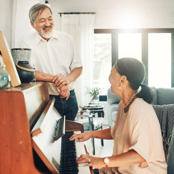 Elderly couple playing piano for music in living room for bonding, entertainment or having fun. Happy, smile and senior Asian man and woman in retirement enjoying keyboard instrument at modern home