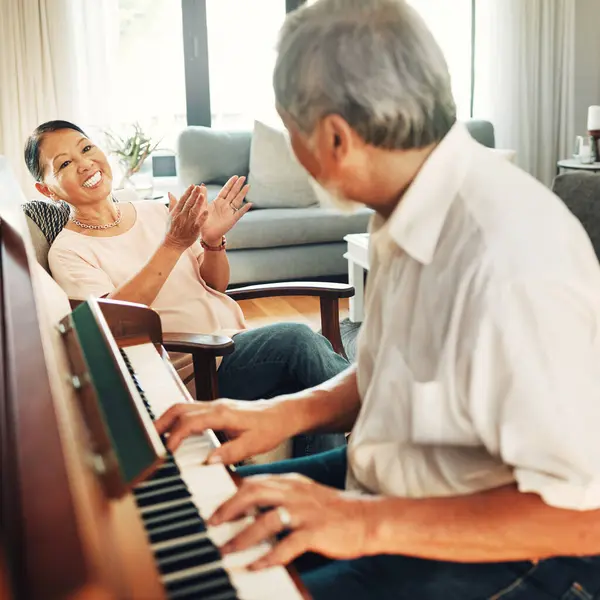 Smile, piano and senior man playing a song to his wife for music in living room with bonding or entertainment. Happy, instrument and elderly Asian couple in retirement enjoy keyboard at modern home