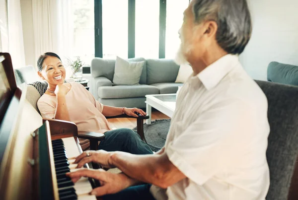 Happy, piano and senior man playing for music in living room with wife for bonding, entertainment or having fun. Instrument, smile and elderly Asian couple in retirement enjoy keyboard at modern home.