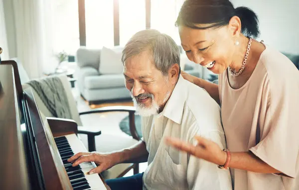 Senior couple playing piano for music in living room for bonding, entertainment or having fun. Happy, smile and elderly Asian man and woman in retirement enjoying keyboard instrument at modern home
