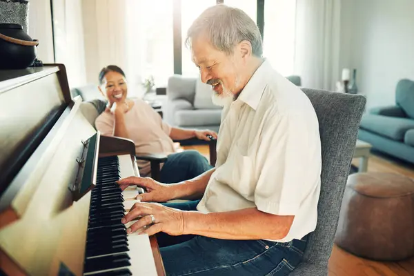 Senior man playing piano for music in living room with wife for bonding, entertainment or having fun. Happy, smile and elderly Asian couple in retirement enjoying keyboard instrument at modern home