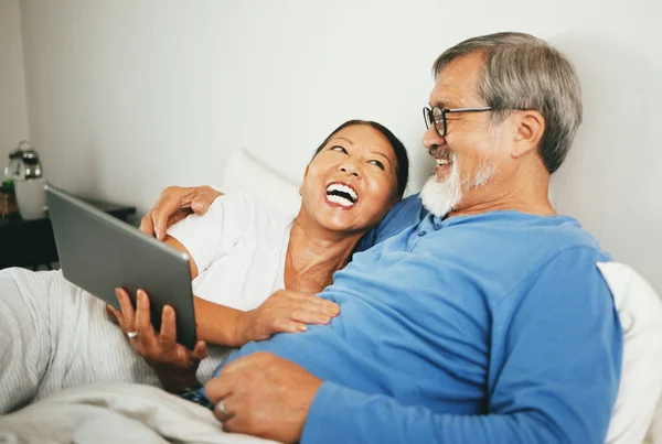 Tablet, mature or happy couple in bed for movie watching on website subscription via internet connection. Meme, home or mature woman laughing at comedy with an Asian man streaming film on tech online.