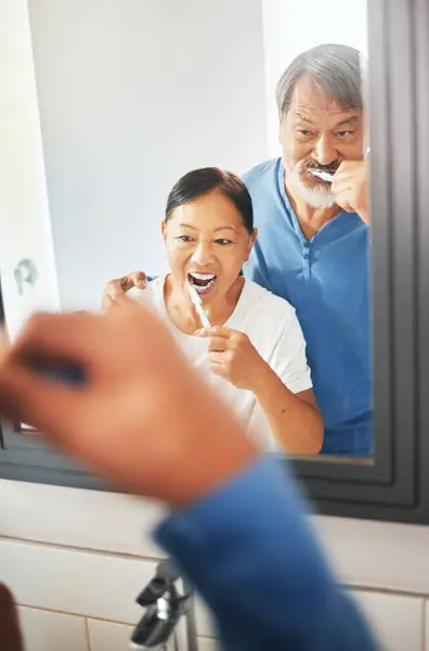 Senior couple, brushing teeth and mirror in bathroom, hygiene and dental, morning routine at home. Healthy people, wellness and oral care with grooming, toothpaste for cleaning mouth and reflection.