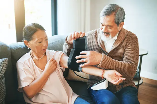 Blood pressure, medical and senior couple in living room with equipment for hypertension. Sick, love and elderly man with healthcare tool for woman in retirement in the lounge of modern home together.