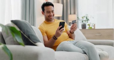 Kredi kartı, telefon ve internetten alışveriş yapan adam rahatlamak için internetli bir evde kanepe satın alıyor. Happy, web sitesi ve internetten satın alan kişi ya da oturma odasındaki kanepeye para yatıran kişi.
