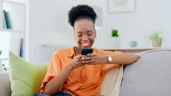 Smile, black woman and typing on smartphone on sofa, update social media post and mobile chat at home. Cellphone, app and download digital games, reading multimedia connection and online subscription.