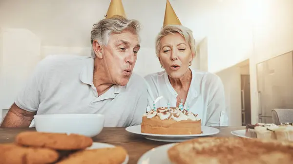 Blowing candles, senior couple and cake for a birthday, celebration party or eating together. Wish, house and an elderly man and woman with sweet food or hungry for a snack together for anniversary.