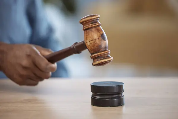 Gavel, hand of lawyer or judge in office for decision, attention or legal advice in justice system. Hammer, desk and person in courtroom, law firm or government agency to stop hearing in human rights.