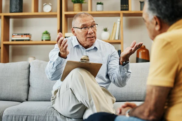Senior man speaking to a psychologist at mental health, psychology and therapy clinic for session. Psychological therapist with clipboard for counseling checklist with elderly male patient in office