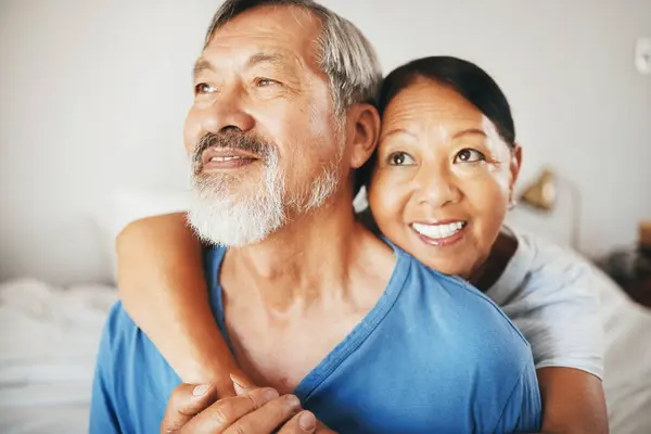 Love, smile and senior couple hugging in the bedroom for bonding, thinking and relaxing together. Happy, care and elderly Asian man and woman in retirement embracing for connection by modern home
