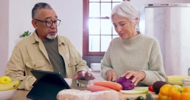 Yemek pişirmek, konuşmak ya da evde emeklilikte sağlıklı bir vejetaryen diyeti için tabletli veya yiyecekli yaşlı bir çift. Çevrimiçi, ırklar arası ya da kıdemli bir kadın mutfakta yaşlı bir adamla ya da yemek tarifiyle bağ kuruyor..