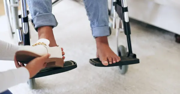 Caregiver, help and shoes of patient in wheelchair, healthcare and assistance in nursing home. Nurse, closeup of hands and take off footwear of person with a disability for support of medical worker.