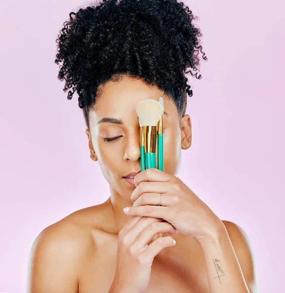 African, woman and brush for makeup on face fro beauty, cosmetic tools or pink background in studio. Cosmetics, artist and person with creative skincare brushes for foundation or powder application.