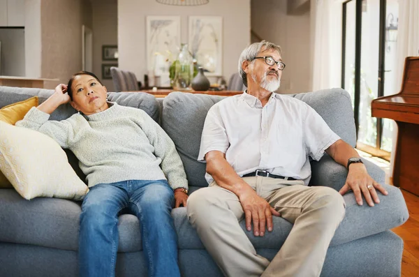 Senior couple, angry and sofa in home living room, thinking or frustrated face for conflict in retirement. Elderly Asian man, old woman and stress on couch with silence, argument or fight in house.