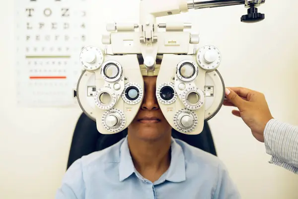 Woman, eye exam and phoropter with optometrist hand, check and lens for vision, wellness and health in clinic. Doctor, eyesight tools and machine for assessment, consultation and glasses in hospital.