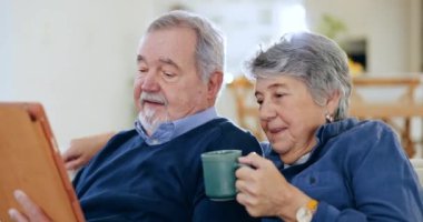 Kahve, tablet ve yaşlı çift bir kanepede konuşuyor, gevşiyor ve sosyal medyada iletişim kuruyor. Mutlu, dijital teknoloji ve emeklilik parşömenindeki yaşlı kadın ve erkek evdeki mobil uygulamayı kullanıyor.