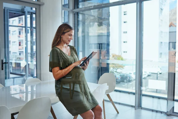 Woman, reading and tablet in office for business, networking or ideas for marketing or sitting on table. Person, touchscreen and happiness at work for communication, conversation or web and pregnant.