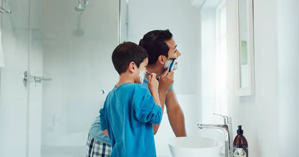 Dad, boy and learning to shave in bathroom with facial cream, skincare routine and support. Father, kid and teaching about cosmetics of cleaning face, beard and foam for love, care and family at home.