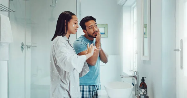 Couple, bathroom and cleaning face with cream, skincare and comic joke with laughing, serum or product. Man, woman and funny with facial oil moisturizer for beauty, wellness or self care in apartment.