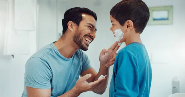 Father, child and learning with shaving cream or teaching a boy a skincare, morning beauty routine and grooming in the bathroom. Shave together, son and dad helping with foam, razor and skin care.