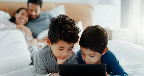 Brothers, children and tablet with parents on bed for game, movies or relax together with mom, dad and laugh. Happy family, boy kids and digital touchscreen for app, learning or development in home.