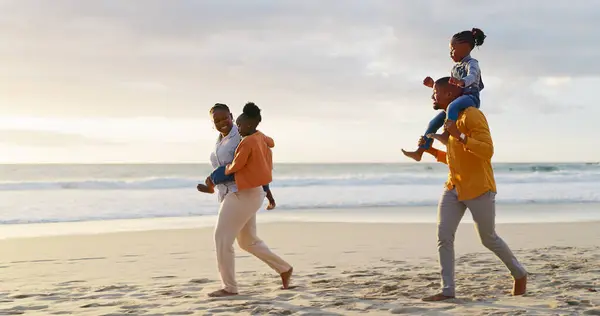 Sunset, happy and walking black family on the beach for bonding, travel or on holiday together. Smile, nature and an African mother and father carrying children while on a walk by the sea on vacation.