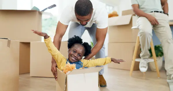 Father, playing and child in a box while moving house with a black family together in a living room. Man and a girl kid excited about fun game in their new home with a smile, happiness and energy.