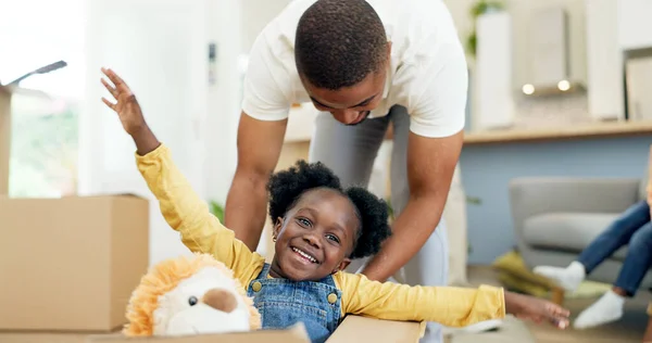 Father, child and playing in a box while moving house with a black family together in a living room. Man and a girl kid excited about fun game in their new home with a smile, happiness and adventure.