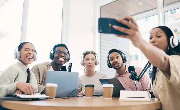Podcast, funny face and group selfie of friends together, live streaming or people recording broadcast on headphones or mic in studio. Radio host team laughing, take photo at table and social media.