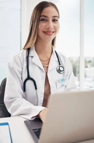 Portrait, doctor and laptop with a woman in a hospital for healthcare, consulting or trust. Medical, smile and a happy young medicine professional typing at a desk in a clinic for cardiology.
