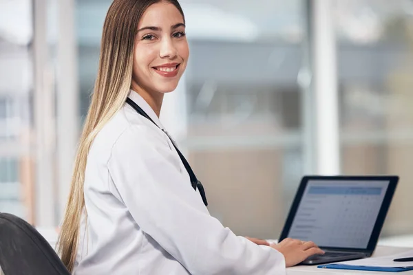 Portrait, doctor and laptop with a woman typing in a hospital for healthcare, consulting or trust. Medical, smile and a happy young medicine professional working at a desk in a clinic for cardiology.