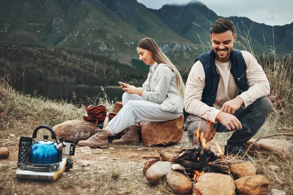 Wood, nature and couple with fire on a camp on a mountain for adventure, weekend trip or vacation. Stone, sticks and young man and woman making a flame or spark in outdoor woods or forest for holiday.