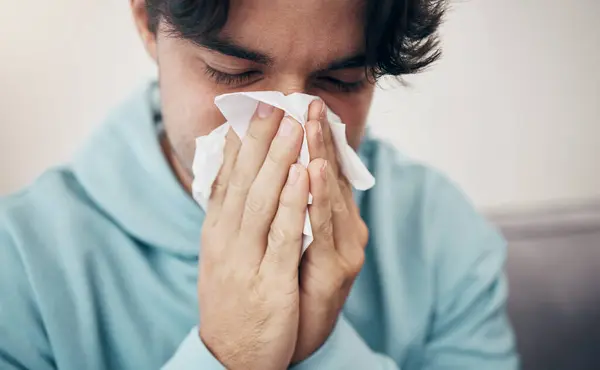 Man, sick and couch with tissue, sickness and virus for infection, sinus and cold symptoms. Sneeze, blowing nose and allergy in living room sofa, hayfever and healthcare for disease, fever or alone.
