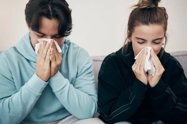 Couple, sick and couch with tissue, sickness and virus for infection, sinus and cold symptoms. Sneeze, blowing nose and allergy in living room sofa, hayfever and healthcare for disease, man and woman.