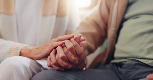 Holding hands, empathy and an elderly couple closeup in their home for love, support or trust in retirement. Hope, healing or sympathy with senior people on a sofa in the living room of their home.