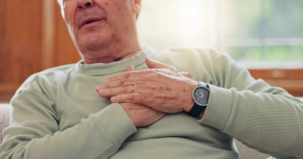 Hands, heart attack or condition with a senior man in pain closeup in the living room of his retirement home. Healthcare, chest or cardiac arrest with an elderly person breathing for lung oxygen.