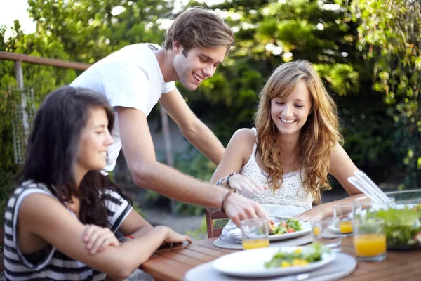 Happy, friends and food serve in backyard with salad at a table with hungry people and smile. Lunch, home garden and group ready for eating with healthy meal together and relax outdoor and laughing.