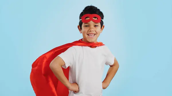 Happy, superhero or face of child with smile to fight in fantasy, dream or cosplay costume in studio. Boy power, brave or strong kid ready to protect freedom or justice with a mask on blue background.