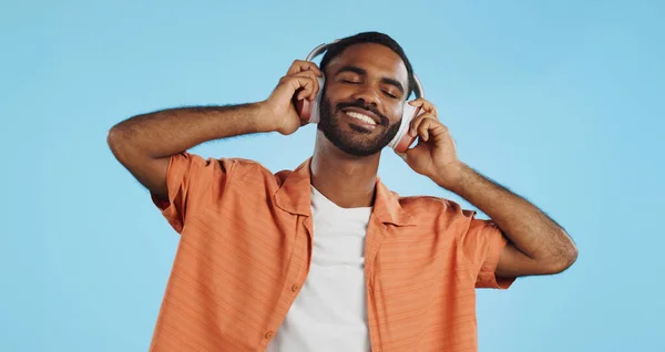 Black man, headphones and dancing to music with happiness and energy in studio on blue background. Techno, rave and fun with audio streaming, dancer is excited with smile and wireless technology.