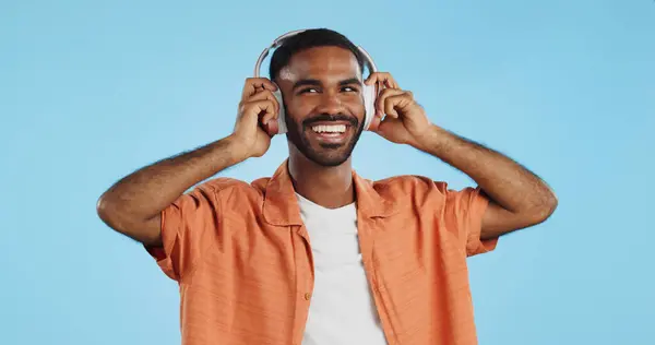 Man, student and headphones for listening to music, dance and mental health for education and wellness in studio. Young african person for audio streaming service, techno or rave on a blue background.