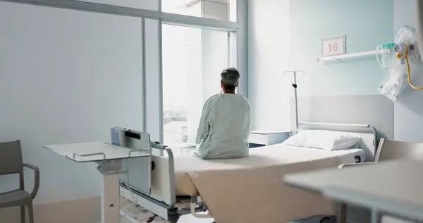 Back, healthcare and a woman on a hospital bed by the window in recovery or waiting for a visit. Medical, cancer and a patient thinking about the future of medicine in a health clinic for treatment.