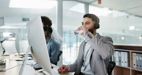 Happy businessman, call center and drinking water in customer service or telemarketing at office. Thirsty man, consultant or agent talking with headphones and drink for online advice, support or help.
