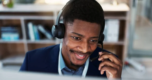 Happy black man, face and headphones in call center, customer service or telemarketing at office. Closeup of African male person, consultant or agent smile and talking for online advice at workplace.