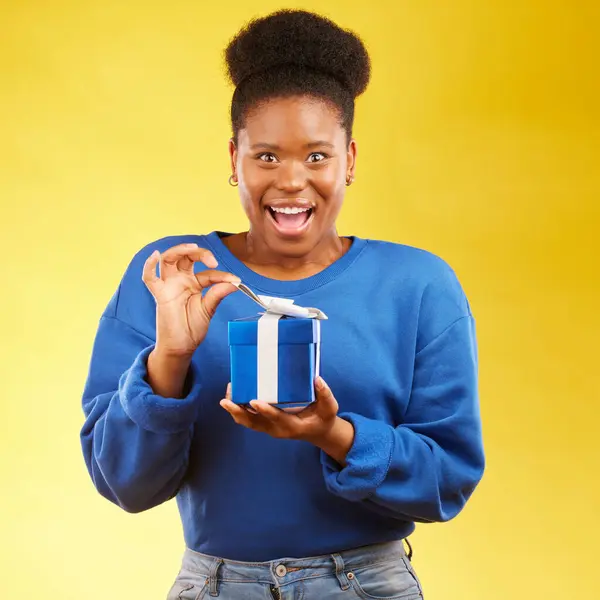 Gift, present and portrait of black woman with a surprise happy isolated in a yellow studio background for a birthday. Shocked, box and excited person to celebrate, party and holiday as a winner.